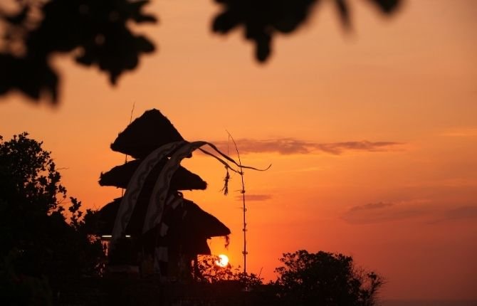 Uluwatu Temple silhouette against orange sunset sky in Bali